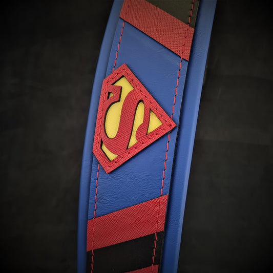 A close-up of the Superdog Collar, a blue and red strong dog collar featuring a yellow and red Superman logo patch stitched onto it, set against a dark background.